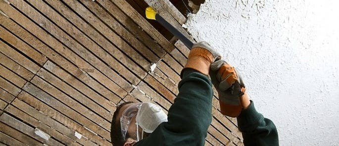 man removing asbestos from a roof with a mask over his face to avoid exposure