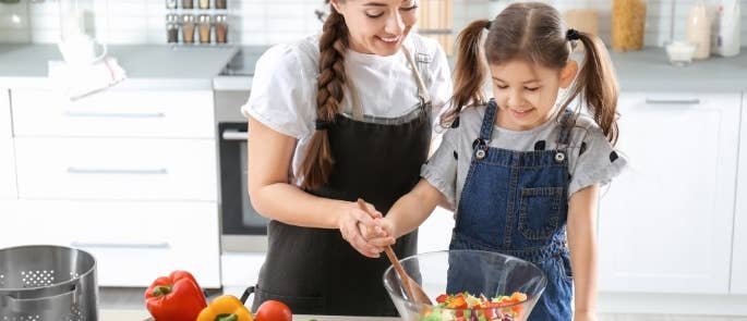 Childminder making salad with young girl