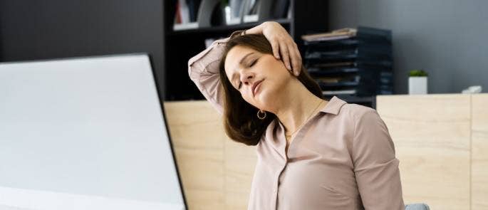 Woman sat at desk and computer screen and doing neck exercises