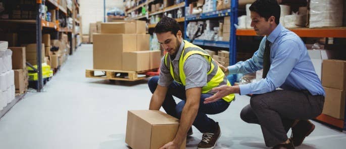 Manager in warehouse providing manual handling lifting training to employee