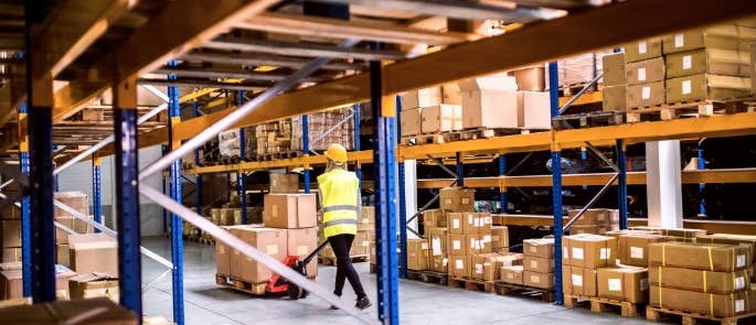 Worker pushing hand forklift in warehouse