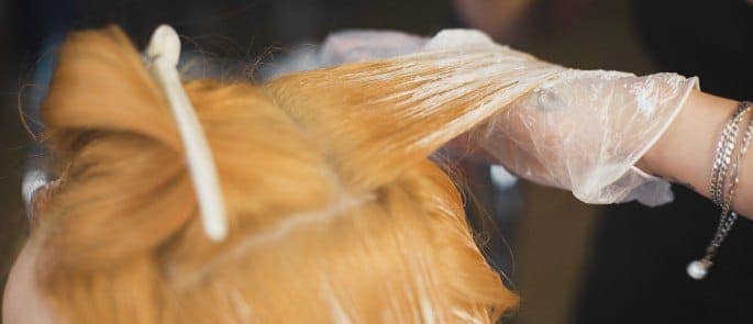 A hairdresser bleaching hair wearing gloves to protect against bleach