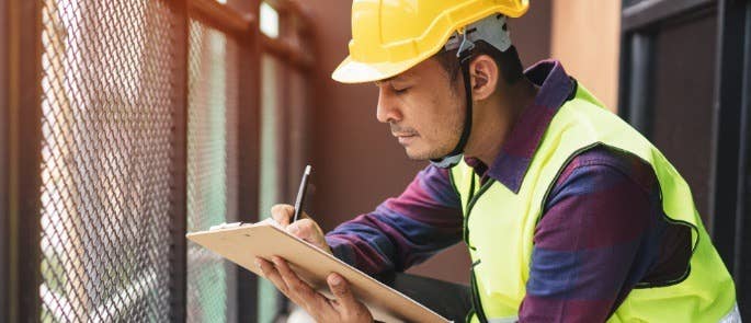 Man in protective clothing at a building site taking notes