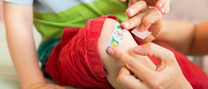 Parent putting a plaster on their child teaching them about first aid