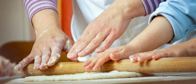 Parent showing child how to roll dough