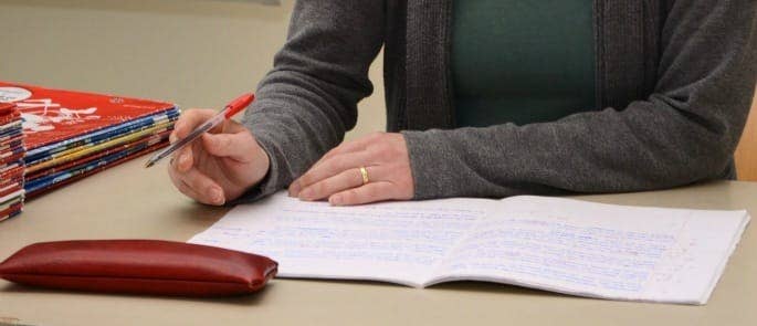 female writing in a notepad on a teachers' desk