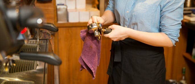 A barista cleaning coffee making equipment as part of a clean as you go policy