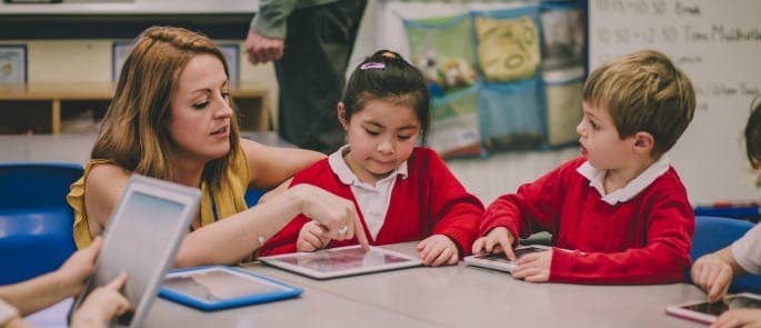 A teaching assistant helping pupils correct their work on a tablet using marking symbols