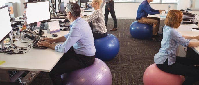 Workers sitting on exercise balls at their desk as part of their wellbeing programme