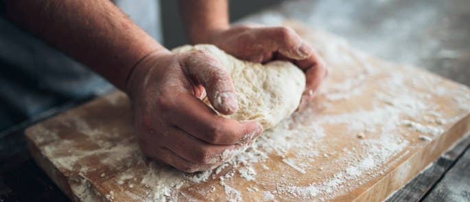 Baker kneading dough and flour on wooden board