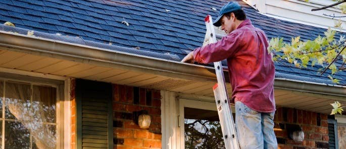 Man standing on a ladder to look at house gutters