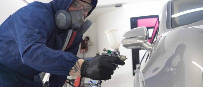 Worker spray painting car and wearing protective equipment