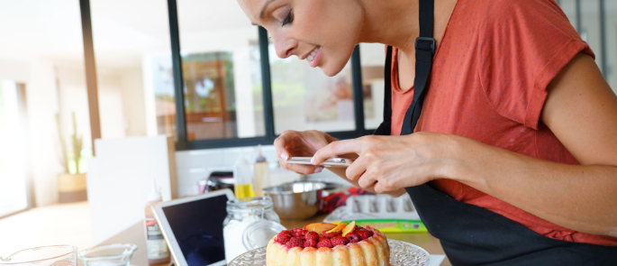 Woman leaning over a cake taking a picture of it on her mobile phone.