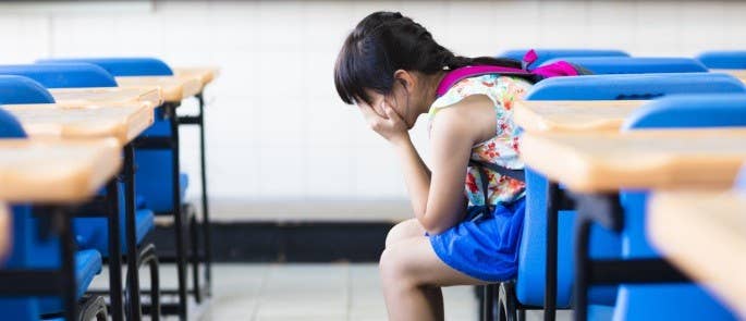 Sad schoolgirl sat down in classroom with head in hands