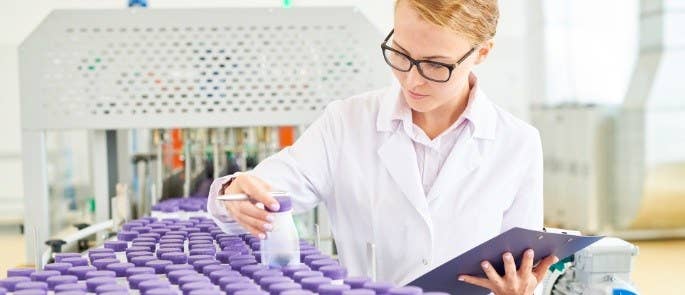 woman wearing white coat holding a clipboard checks a bottle label from the assembly line in a factory.