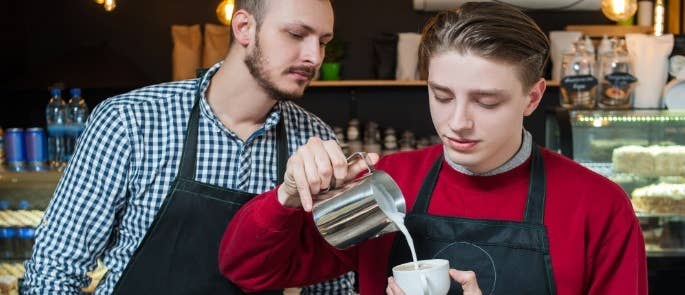 Manager oversees young male worker making coffee for customer