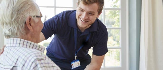 Young male care worker brings elderly man his lunch.