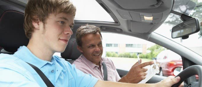 Driving instructor sits in passenger seat with young male who is learning to drive