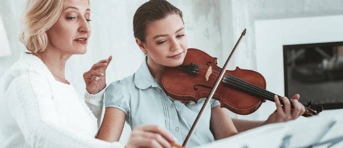 Older lady teaches young girl how to play violin.