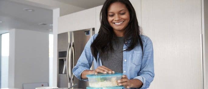 Woman in her kitchen at home putting leftover food into plastic containers