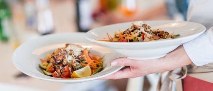 Waiter carrying two bowls of food to a table in a restaurant