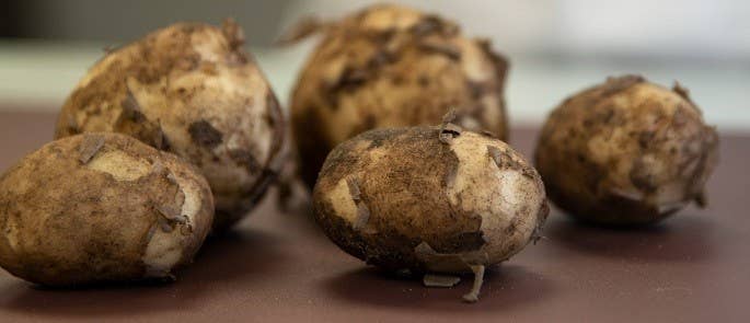 Dirty potatoes on a brown chopping board