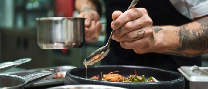 Close-up of chef drizzling sauce onto plate of food