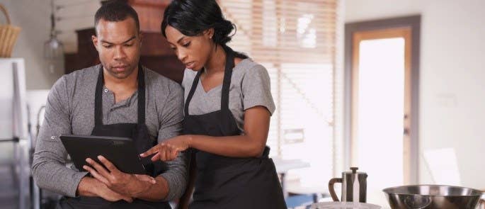 Two deli workers in aprons looking at a tablet