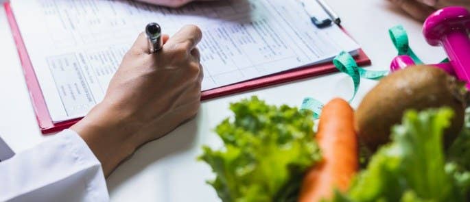 Close up shot of a nutrition plan with vegetables on the desk nearby