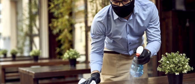 Employee spraying table with disinfectant