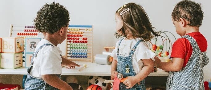 Three early years children turning around to look at toys in playroom.