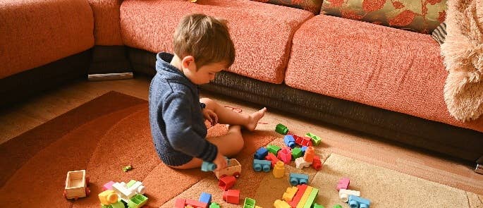 Young child playing with bricks on living room floor.