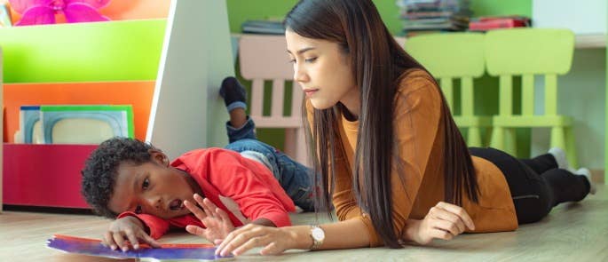 Childcare worker trying to engage with stubborn child on floor.