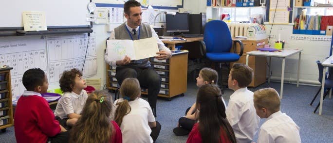 Male teacher explaining book to class of primary school children