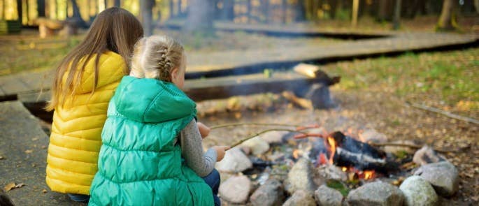 Two children cooking sausages on sticks around a campfire