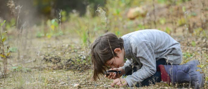 Child examining ground with magnifying glass