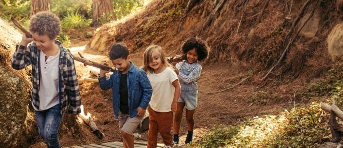 Children working together to carry log along forest path