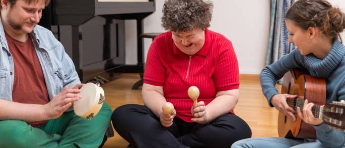 Adult music therapy session with participants using percussion instrument and therapist accompanying on guitar