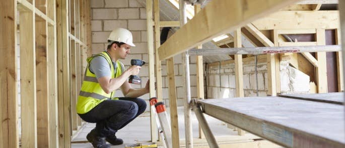 Male construction worker using a drill in a partly-constructed house