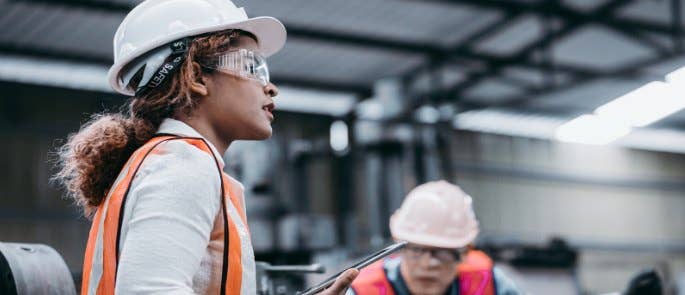 Woman in PPE holding a tablet and talking to colleagues