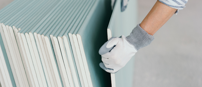 A construction worker with plasterboard  that contains gypsum.