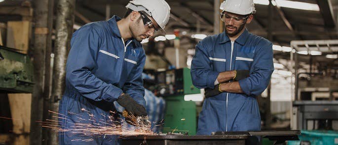 an employee using a grinding wheel and a colleague overseeing the process 