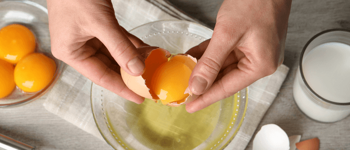 Someone cracking raw eggs into a bowl.