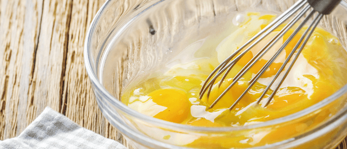 Someone in the process of whisking raw eggs in a bowl