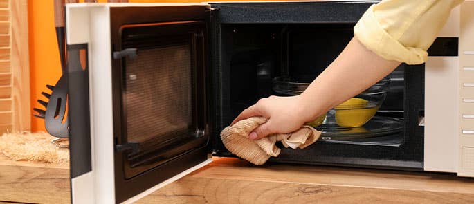 The inside of a microwave being cleaned with lemons and water and a cloth