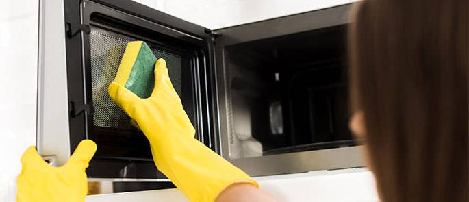 Microwave door being cleaned with a sponge