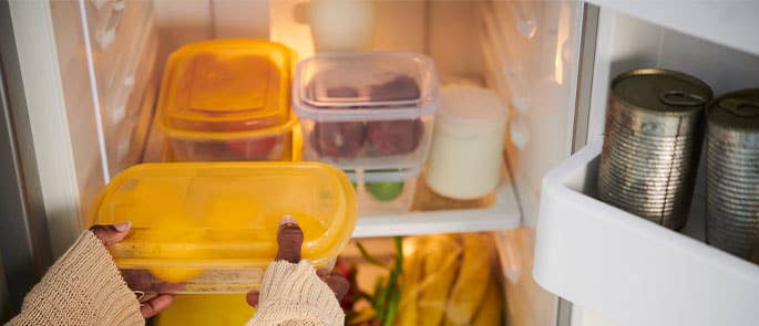 Tub of leftover food being place on a fridge shelf
