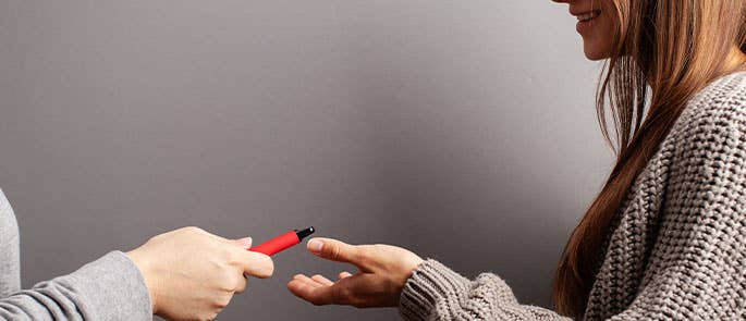 Young girl being handed a bright red vape