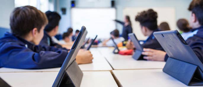Children using iPads or tablets in a classroom and teacher using a smart board to teach