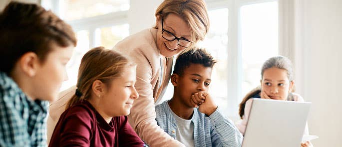 Teacher helping group of young students in classroom